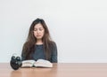 Closeup asian woman sitting for read a book with boring face emotion on wood table and white cement wall textured background with Royalty Free Stock Photo