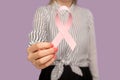 Closeup of woman in striped blouse holding pink ribbon, symbol of breast cancer awareness