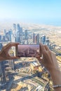 Closeup of woman tourist hand taking photo of Dubai city with smartphone camera from Burj Khalifa tower.