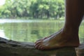 Closeup of a woman& x27;s bare feet on a wooden log sunlit pond and trees blurred background