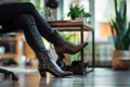 closeup of womans feet in open workspace with sleek leather boots under desk