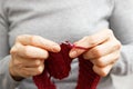 Closeup womans hands knits red burgundy wool yarn with knitting needles.