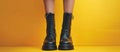 Womans Legs in Black Boots on Yellow Background