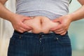 Closeup womans stomach wearing jeans, grabbing onto excessive fat using fingers, belly button revealed, weightloss Royalty Free Stock Photo