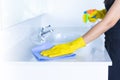 Closeup women hand maid or charwoman cleaning modern new basin in bathroom. Water tap clean using yellow gloves and blue cloth