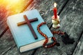 Closeup of wooden Christian cross on bible, burning candle and prayer beads on the old table. Royalty Free Stock Photo