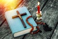 Closeup of wooden Christian cross on bible, burning candle and prayer beads on the old table. Royalty Free Stock Photo