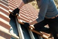 Closeup of worker hands installing yellow ceramic roofing tiles mounted on wooden boards covering residential building roof under Royalty Free Stock Photo