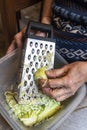 Closeup wrinkled hands grating the zucchinis in kitchen