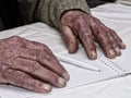 Closeup of the wrinkled hands of man holding pen and paper, wearing a green sweater Royalty Free Stock Photo