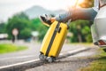 Closeup of yellow luggage and woman legs relaxing on back of car with road background. Road trip and holiday vacation concept.