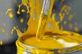 closeup of yellow paint splashing as brush dips into can