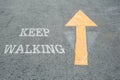 Closeup yellow painted arrow sign on cement street floor with white keep walking word textured background