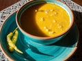 Closeup yellow puree soup in a white bowl, salted peppers and white sauce