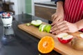 Closeup of young asian man with apron cutting red and green apple kiwi orange on wooden board Royalty Free Stock Photo