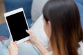 Closeup young asian woman sitting and using mockup of tablet computer with display blank screen on sofa at home. Royalty Free Stock Photo