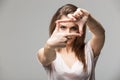 Closeup of young beautiful brunette woman making frame with her fingers, over gray background Royalty Free Stock Photo