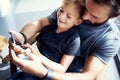 Closeup of young boy sitting with father and using smartphone in modern sunny place. Horizontal, blurred background.