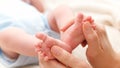 Closeup of young caring and loving mother massaging and stroking little feet of her newborn baby son lying in bed Royalty Free Stock Photo