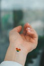 Closeup of young caucasian millennial hippie woman with painted rainbow flag in heart shape painted in wrist. Rainbow