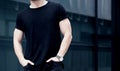 Closeup of young caucasian muscular man wearing black tshirt and jeans posing in center of modern city. Blurred Royalty Free Stock Photo