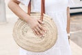 Closeup of young caucasian woman in white madeira lace dress holding round straw bag with leather straps. Hands with Royalty Free Stock Photo