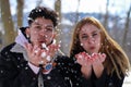 Closeup of a young couple of a latin boy and a caucasian blonde girl blowing snow from their hands in winter