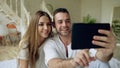 Closeup of Young cute and loving couple having video chat holding smartphone and chatting to friends sitting in bed at Royalty Free Stock Photo