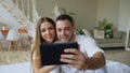 Closeup of Young cute and loving couple having video chat holding smartphone and chatting to friends sitting in bed at Royalty Free Stock Photo