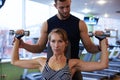 Young determined woman flexing biceps with personal trainer in g