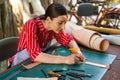 Closeup young female leather maker using a cutter knife to cut a piece of leather sheet according to the design to bring out to