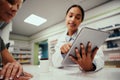 Closeup of young female pharmacist hand holding digital tablet wearing labcoat and standing behind counter guiding