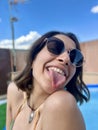 closeup of a young girl in sunglasses sticking out her tongue at camera while enjoying in the pool at home in summer Royalty Free Stock Photo