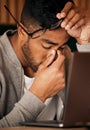 Closeup of young indian man feeling stressed while sitting alone and using a laptop to browse the internet. Mixed race Royalty Free Stock Photo