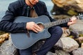 Closeup of young man playing acoustic guitar on beach surrounded with rocks on rainy day Royalty Free Stock Photo