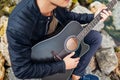 Closeup of young man playing acoustic guitar on beach surrounded with rocks on rainy day Royalty Free Stock Photo