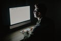 Closeup of young man sitting and using blank screen computer in dark room. hacker or programmer in dark room. Royalty Free Stock Photo