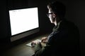 Closeup of young man sitting and using blank screen computer in dark room. hacker or programmer in dark room. Royalty Free Stock Photo