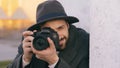 Closeup of young paparazzi man in hat photographing celebrities on camera while spy behind the wall Royalty Free Stock Photo