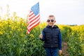 Boy standing with the american flag on the green and yellow field celebrating national independence day. 4th of July concept Royalty Free Stock Photo