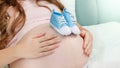 Closeup of young pregnant woman lying in bed and holding blue newborn baby boots on big belly. Concept of pregnancy Royalty Free Stock Photo