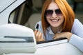 Closeup of a young redhead woman driver correcting her makeup with dark red lipstick looking in car rearview mirror behind Royalty Free Stock Photo