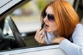 Closeup of a young redhead woman driver correcting her makeup with dark red lipstick looking in car rearview mirror behind Royalty Free Stock Photo