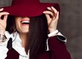 Closeup of young stylish woman brunette in black jacket and white shirt pulls down hat brim hiding her eyes and laughs Royalty Free Stock Photo