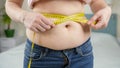 Closeup of young woman with fat belly measuring her waistline. Concept of dieting, unhealthy lifestyle, overweight and Royalty Free Stock Photo