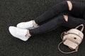 Closeup of a young woman`s legs in ripped fashionable black jeans in leather stylish sneakers with snake pattern