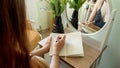 Closeup of young woman sitting at mirror in bedroom and writing in notebook. Female secrets, elegance, education