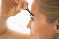 Closeup on young woman tweezing eyebrows