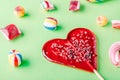 Closuep shot of a heart-shaped lollipop and other candies on a green surface