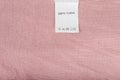 Clothes label says 100% cotton on pink textile background, close up